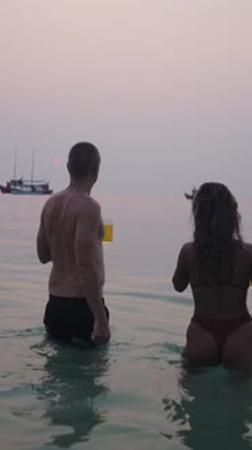 Couple Standing in Ocean at Sunset Near Boats