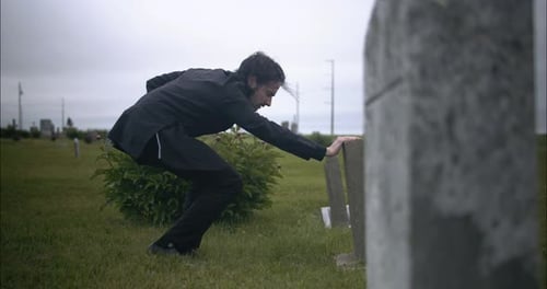 Sad young man kneeling, grieving over lost loved on in cemetery.