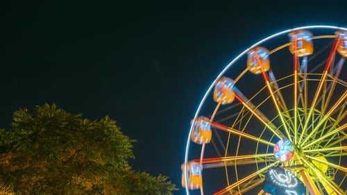 Rotating In Natural Motion Effect Illuminated Attraction Ferris Wheel In City Amusement Park On