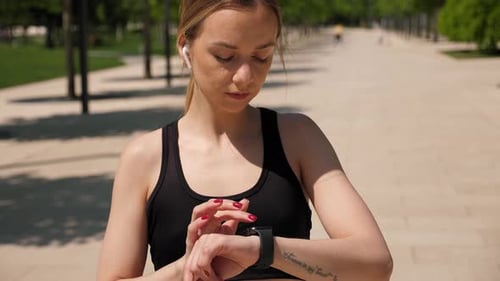 Nahaufnahme einer Frau, die während eines morgendlichen Trainings im Park eine Smartwatch benutzt