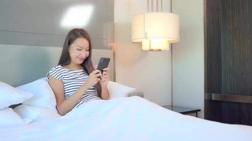 Young Woman Relaxes in Bed with Smartphone