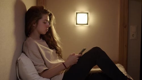 Young Woman Uses Cell Phone in Bed at Night