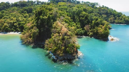 Tropical island covered in trees surrounded by turquoise sea water and beaches