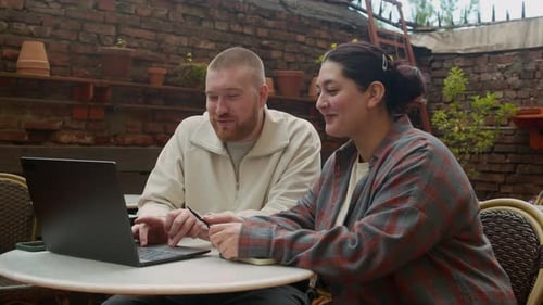 Diverse Employees Discussing Work Sitting by Laptop at Table in Outdoor Cafe