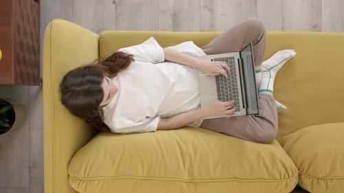Top Down View of Young Woman Working on Laptop While Lying on Couch Freelancer Girl Work From Home