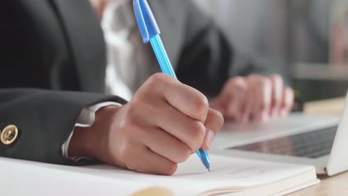 Close Up Of Businessman's Hand Writing On Notebook While Working With Laptop Computer