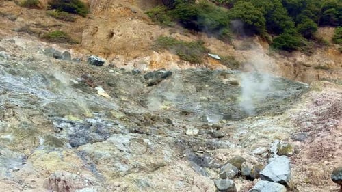 Steam rising from a sulfur-covered rocky slope in a volcanic region,