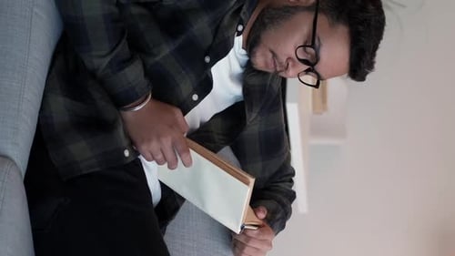 Man Reading Book While Sitting on Couch Indoors