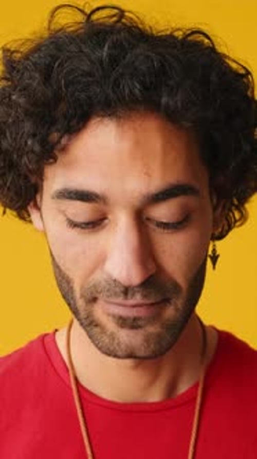 Close-up, man raises his head and looks at camera isolated on yellow background in studio