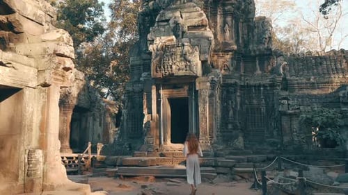 Following a young woman as she walks through ancient carved temple ruins of Ta Prohm, Cambodia