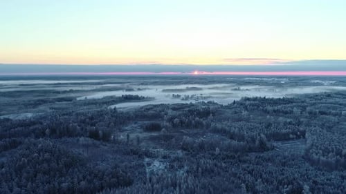 Stunning sunset or sunrise on nordic snowy and foggy landscape and forest. Aerial drone flyback view