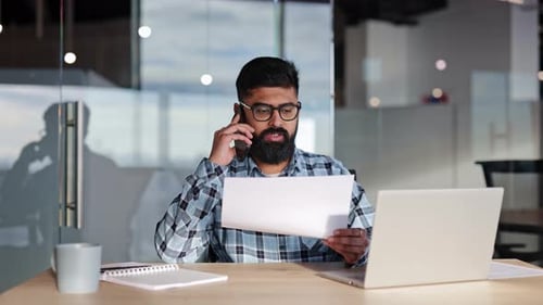 Businessman Reviews Documents While Talking on Phone in Modern Office