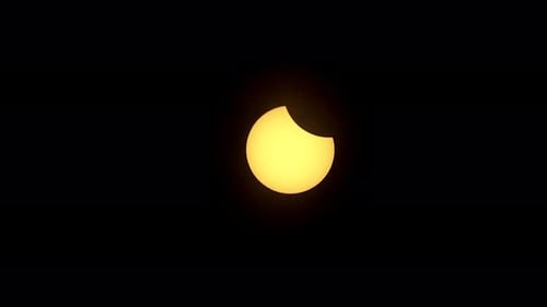 Die teilweise verfinsterte Sonne bewegt sich durch den Himmel mit vorbeiziehenden Wolken.