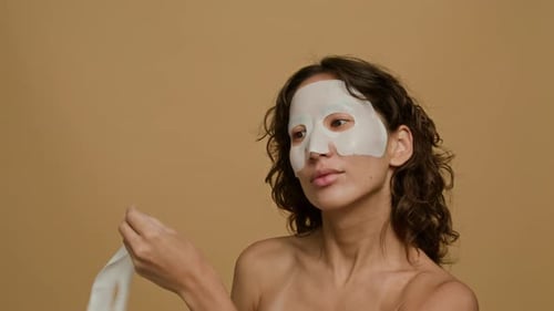 Brunette Girl Removing Sheet Mask from Her Face and Smiling for Camera in Studio