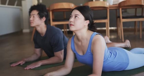 De antebrazos, pareja asiática en estudio, mujer con tanque levantando cofres para extender la columna vertebral sobre colchonetas