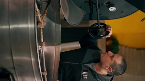 Vertical Video Coffee Roasting Factory Worker Stands Near the Roasting Machine and Monitors the