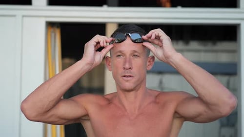 Young attractive swimmer puts on his swimming goggles frontal close up
