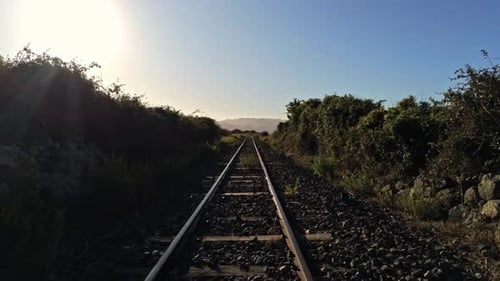 Bodennahe Drohnenaufnahme verlassener Bahngleise, die in den Sonnenaufgang führen.