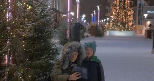 Mom and Kid Making Winter Selfie in the Street with Christmas Illumination