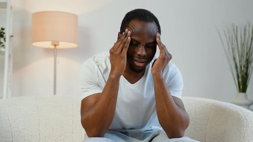 Man With Headache Sitting on Couch Indoors