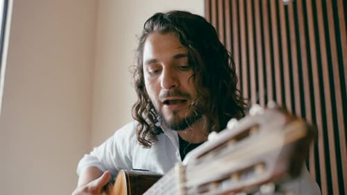 Long Haired Male Musician Playing Classical Guitar and Singing