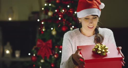 Excited Woman Opens Christmas Present by Tree