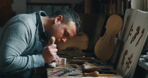 Slow motion of master artisan luthier painstaking detailed work on wood violin in a workshop. Shot
