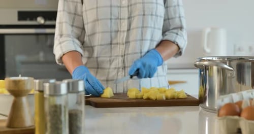 Gros plan des mains dans des gants bleus tranchant des pommes de terre sur une planche à découper