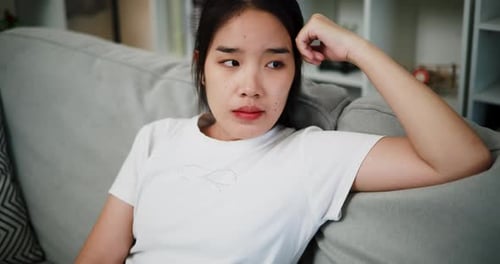 Asian woman thinking about something on the sofa at home.