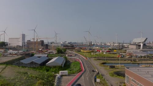 Cars are Driving on a Road Splitting a Port Area with Warehouses and Cranes in Antwerp Wind Turbines