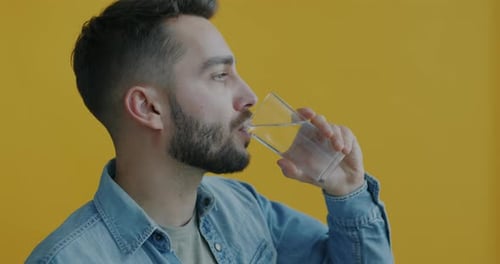 Seitenansicht eines jungen Mannes, der Wasser aus Glas trinkt und ein gesundes Getränk auf gelbem Hintergrund genießt