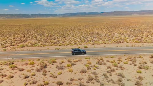 Cars going by the empty road in the sunny desert.