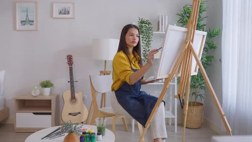 Asian young talented woman artist coloring on painting board in house.
