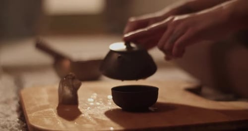Woman Pours Steaming Tea in a Dark Room