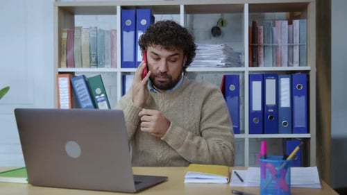 Man Working at Desk on Laptop Making Call