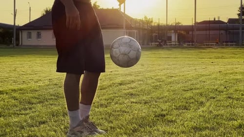 Male Feet of Professional Footballer Kicking Ball at Green Field Legs of Young Man Juggling Soccer