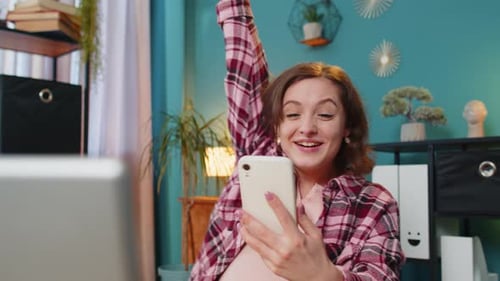 Woman Celebrates Success Using Smartphone at Home