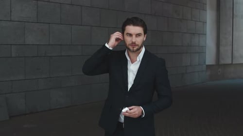 Serious Businessman Putting on Wireless Earphones at City Street. Handsome Male Professional
