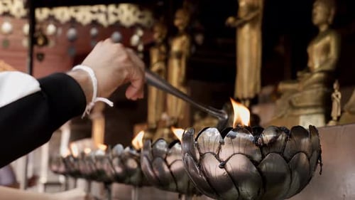 People are filling up oil into the candle holders in a Buddhist temple with a belief that this will