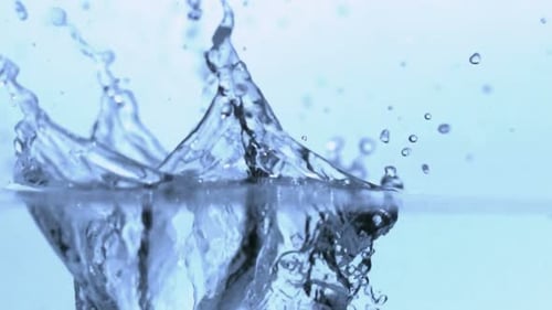 Ice cubes drop into clear water splashing around