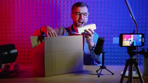 Young Male Technology Blogger Recording Video Blog or Vlog Review of New Smartphone at Home Studio