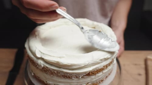 A young woman is spooning white cream onto the top of the cake.