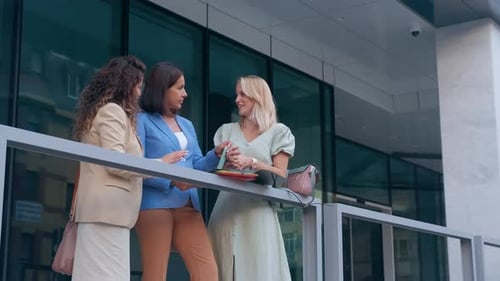 Group of businesswomen standing outside in front of modern office discussing business plans.