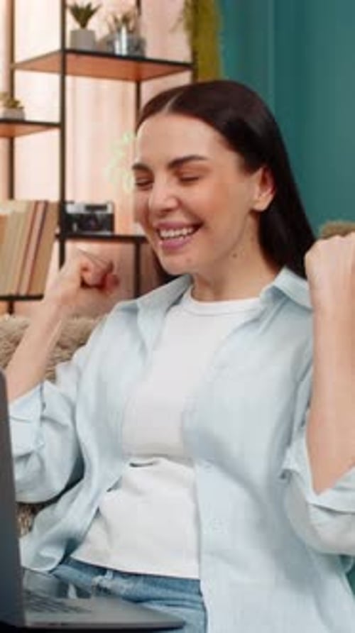Excited woman using laptop in her living room