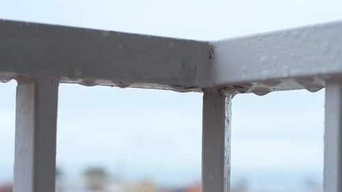 Regentropfen fallen auf das Balkongeländer, wenn es regnet. Nahaufnahme.