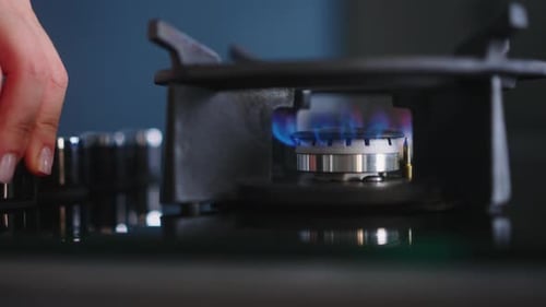 Human Hand Turns on Kitchen Cooktop Gas Burner and Natural Gas Ignites Burns with Blue Flame Person