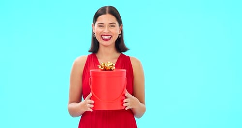 Excited woman, face and gift box in studio, happiness or giving by blue background with smile