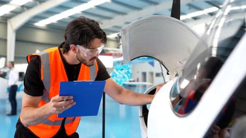 Focused Male Technician Inspecting a Small Aircraft Inside a Bright Hangar