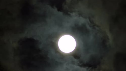 Dramatic clouds moving behind glowing full moon at night