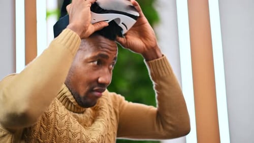 A black man putting on VR glasses in an office and starts exploring virtual reality
